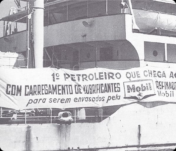 Imagem histórica em preto e branco de navio com faixa sobre carregamento de lubrificantes Mobil.