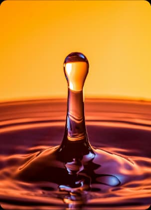 Gota de óleo lubrificante em close-up sobre superfície líquida em tons de laranja e dourado.