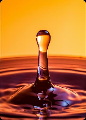 Gota de óleo lubrificante em close-up sobre superfície líquida em tons de laranja e dourado.