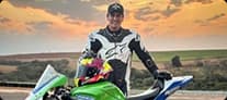 Leandro Melo usando boné e macacão Mobil Super Moto em ambiente externo com céu azul.