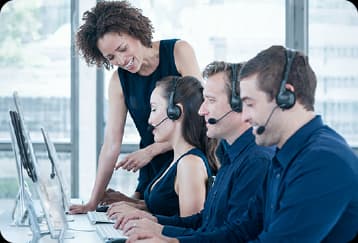 Equipe de atendimento de duas mulheres e dois homens com fones de ouvido trabalhando em computadores em uma central de suporte.