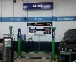 Oficina automotiva com carros em manutenção, elevadores e galão Mobil Super da Troca Inteligente.